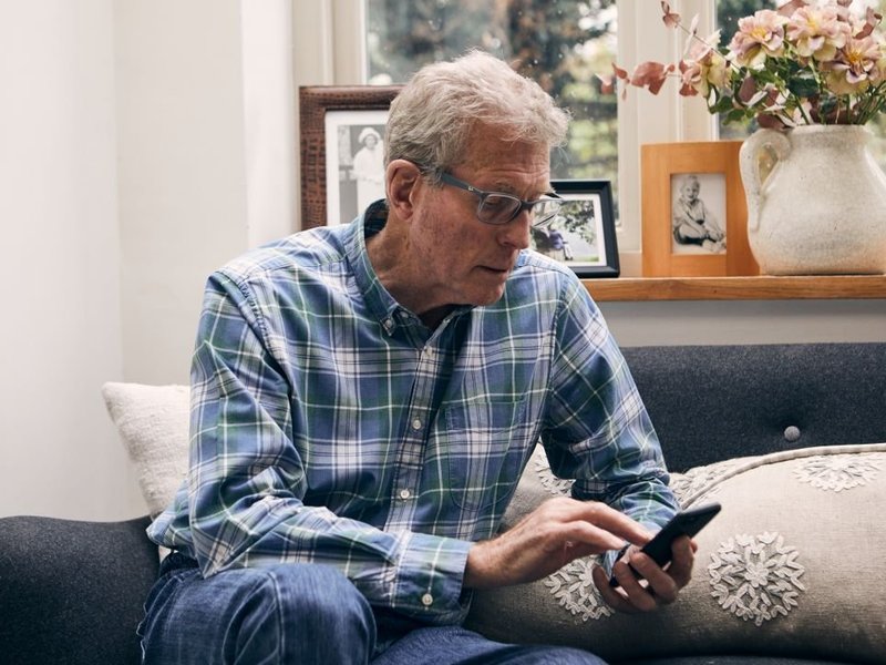 A man is sat on a sofa looking at a mobile phone