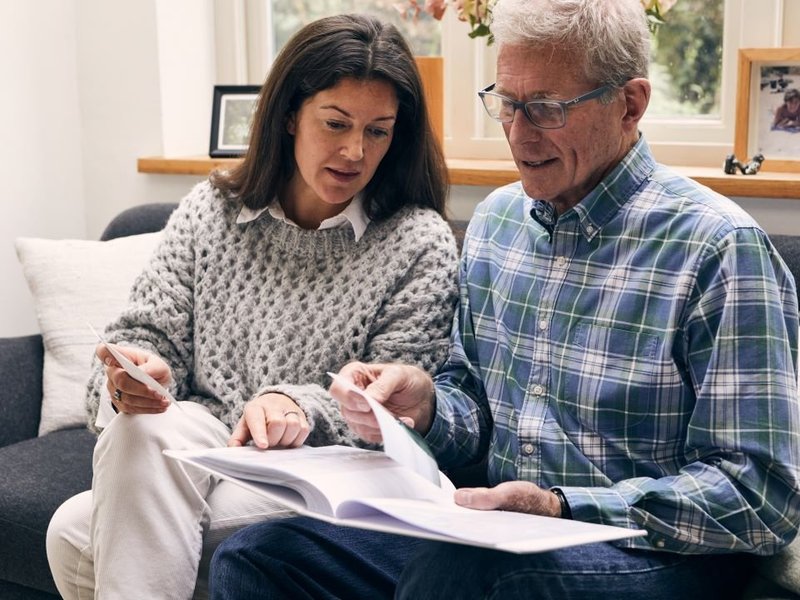 A man and a woman are sat on a sofa looking at a photo album together