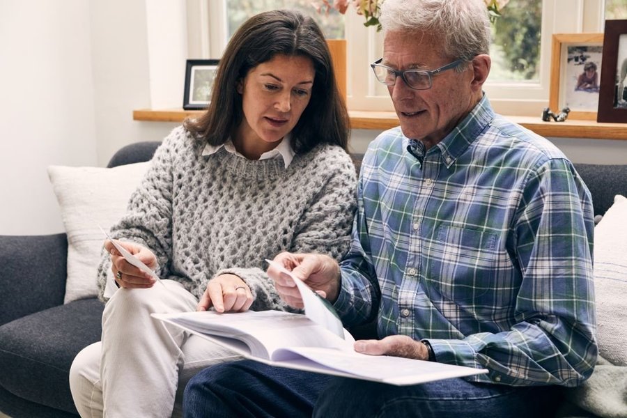 A man and a woman are sat on a sofa looking at a photo album together