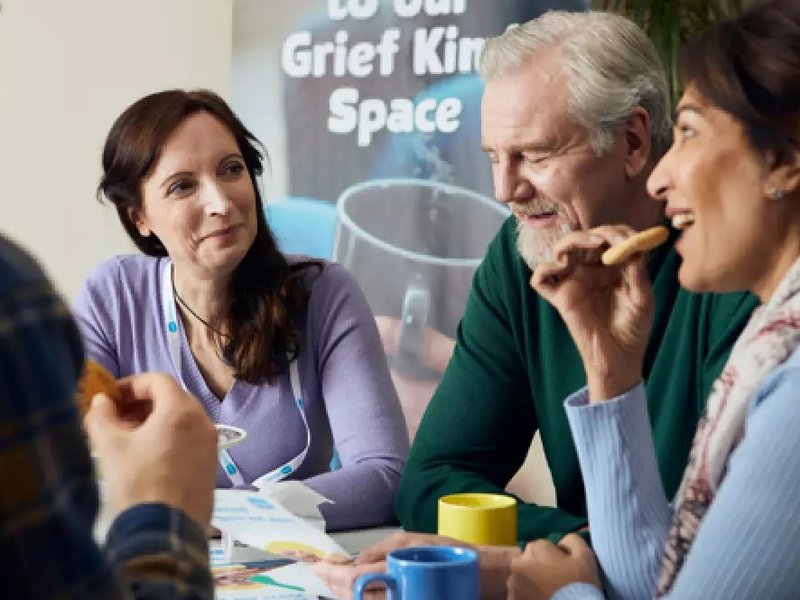 A mixed group of people are talking and drinking tea in a Grief Kind space