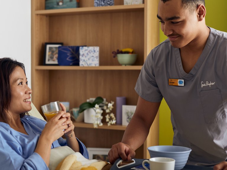A Sue Ryder hospice volunteer serving breakfast to a patient in bed