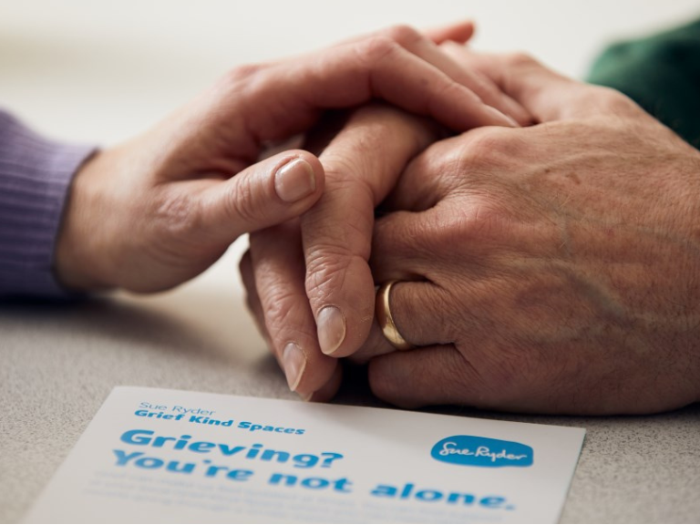 Close up of two people holding hands on a table with a grief advice booklet in front of them