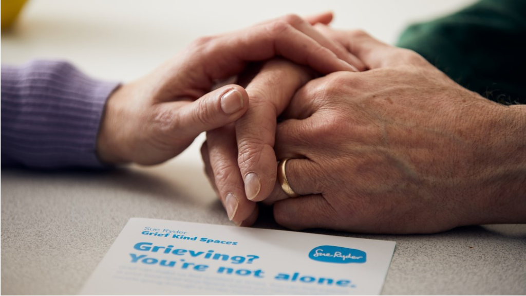 Close up of two people holding hands on a table with a grief advice booklet in front of them