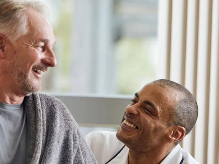 Man in dressing gown looks down at nurse crouching beside him