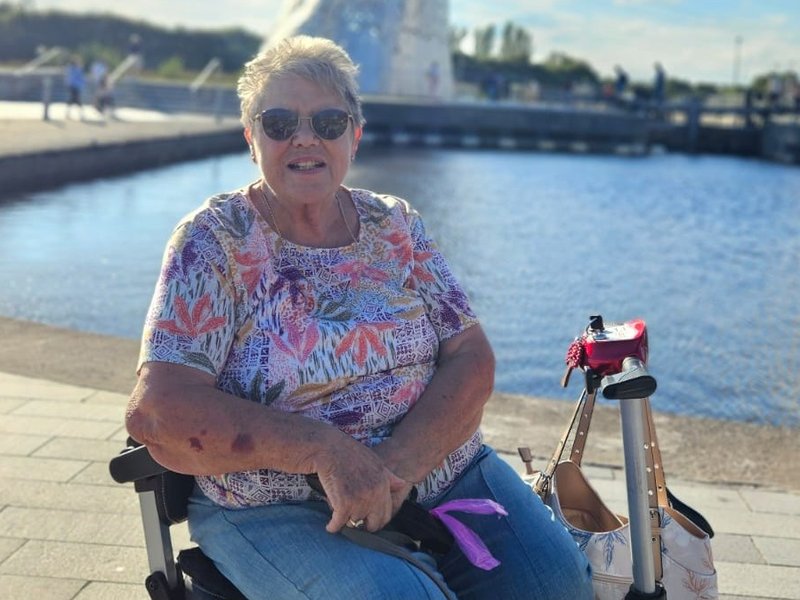 A photo of Rosemary sat outside in the sunshine by a lake
