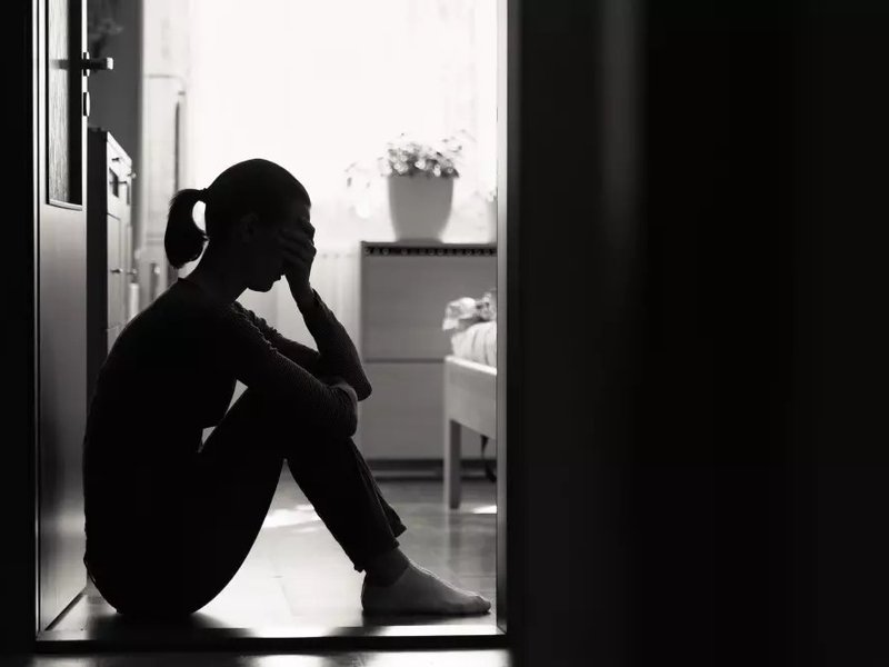 A black and white photograph of a woman sitting down holding her head in her hands.