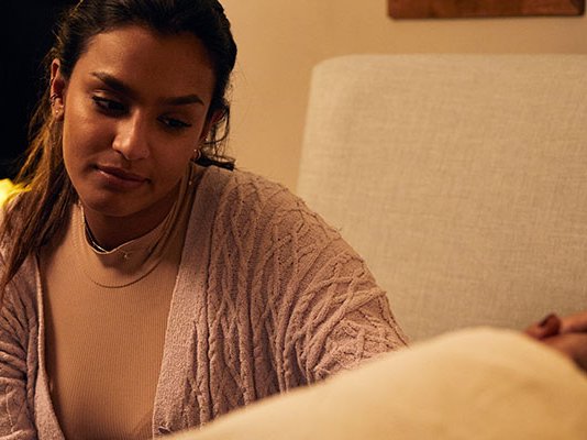 A daughter comforting her bed-ridden father, by stroking his head at his bedside