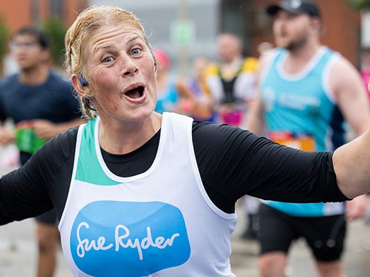 A Sue Ryder runner celebrating with their hands in the air