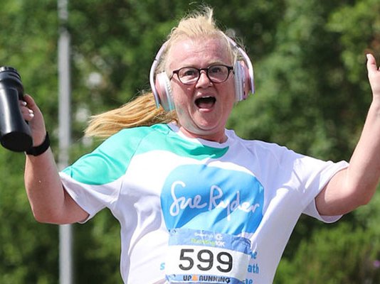 A smiling Sue Ryder runner holding her hands up in the air while racing