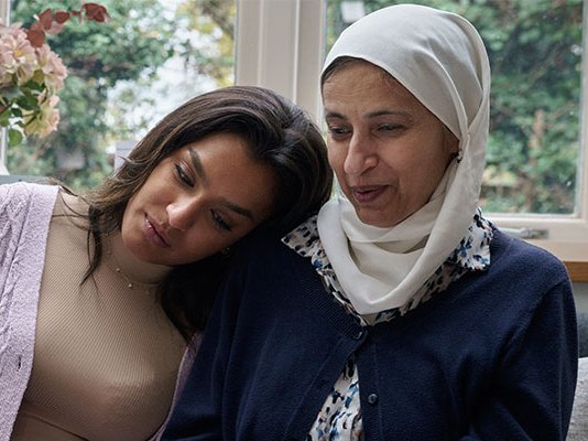 A grieving daughter puts her head on her mother's shoulder
