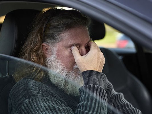 A grieving man alone and crying in his car, with his hand to his face