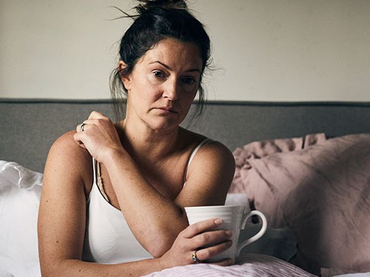 A grieving woman sitting up in bed, holding a cup of tea