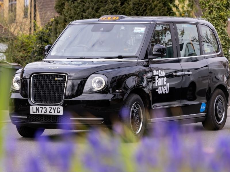 Black London taxi with ‘The Cab Fare-well’ Sue Ryder campaign branding parked on a residential street