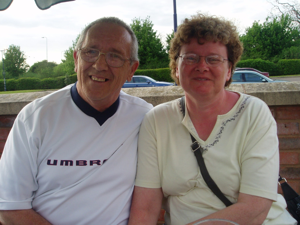 A recent color photo of the Debbie and Doug sitting together outdoors, both smiling.