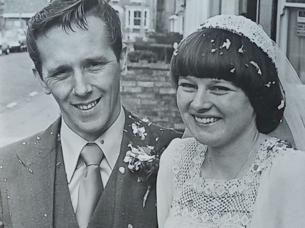 A black and white wedding photo of a smiling couple sitting together outdoors, both looking content.