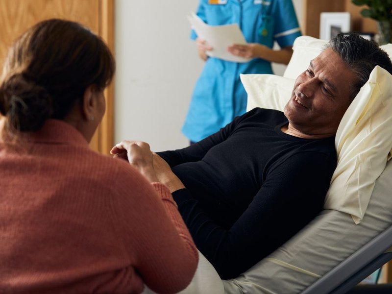 A relative comforts a patient in a hospice bed, with a Sue Ryder Nurse behind them