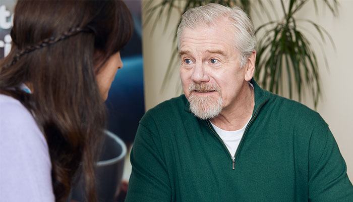 An older man holding a cup of tea, talking to a Sue Ryder grief support volunteer