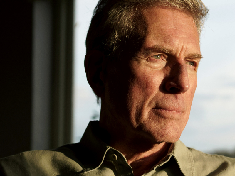 Man looks solemnly into the distance . A shadow takes up much of his face.