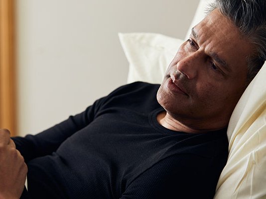 A woman holds her partner's hand to comfort him at his bedside