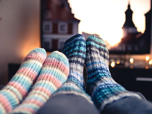 A close up of two pairs of feet in thick socks, next to each other in a living room