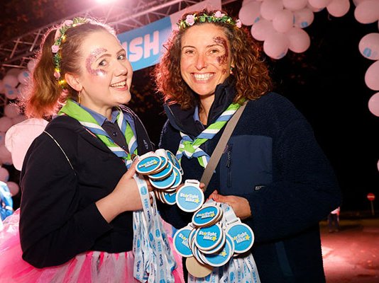 Two smiling Sue Ryder Starlight Hike volunteers, holding medals near the finish line