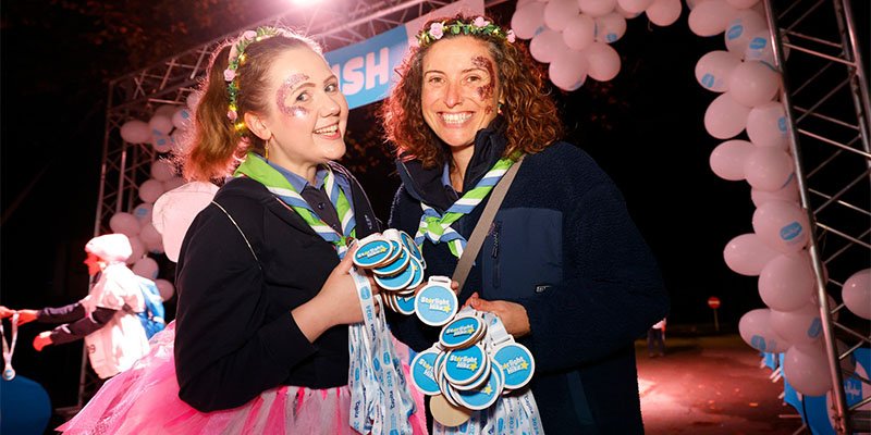 Two smiling Sue Ryder Starlight Hike volunteers, holding medals near the finish line