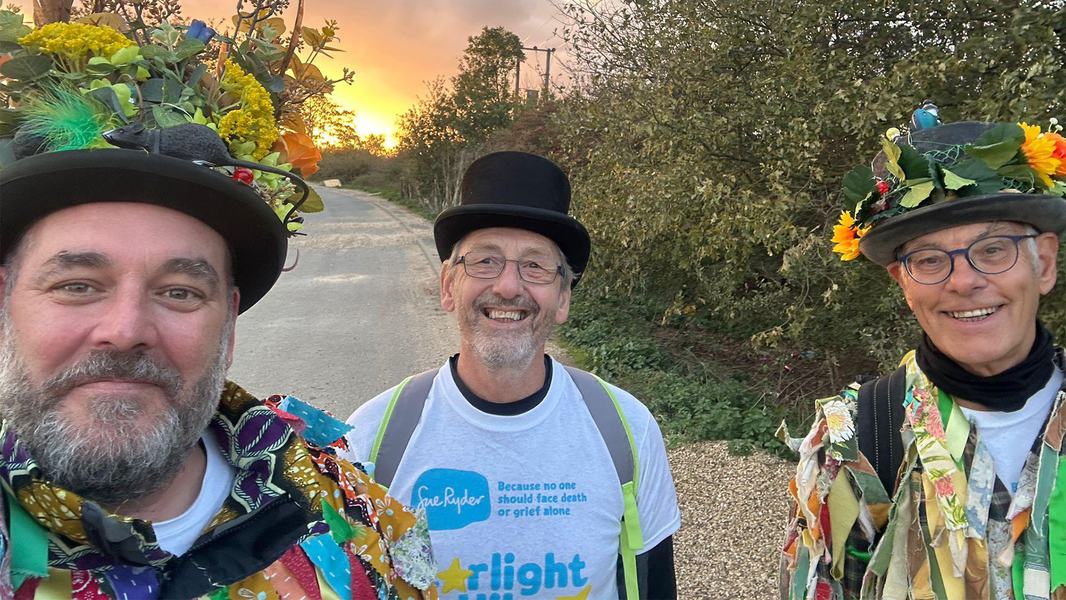 Three Starlight Hike walkers in morris dancing outfits, with the sunset behind them