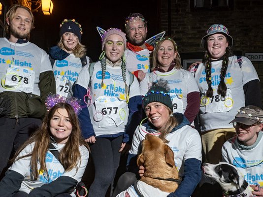 A group of Starlight Hike walkers in neon clothing, surrounded by their dogs