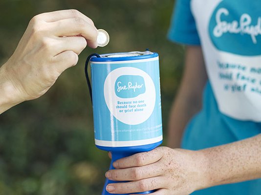 A close up a Sue Ryder volunteer holding a collection tin for a person to place a coin into