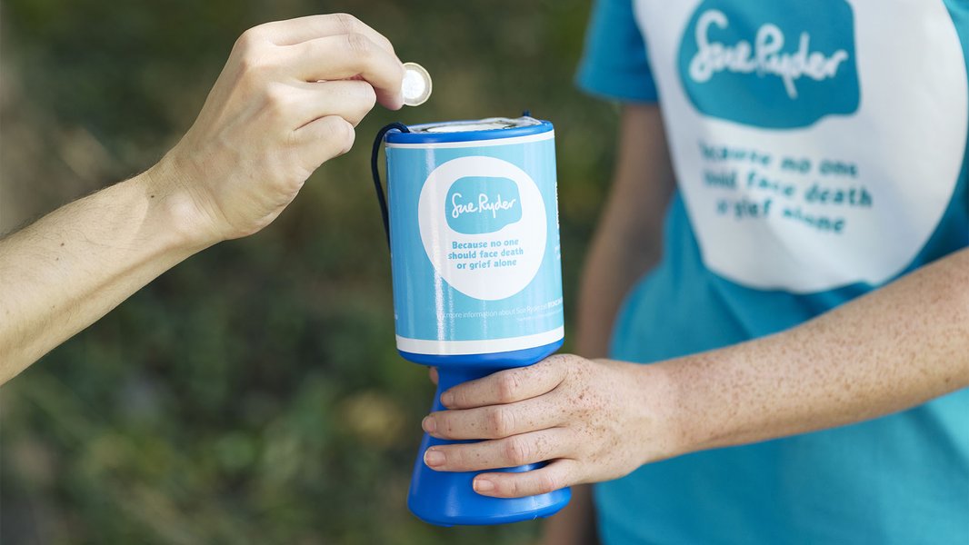A close up a Sue Ryder volunteer holding a collection tin for a person to place a coin into