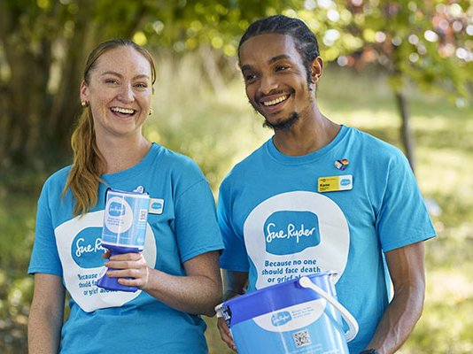 A male and female Sue Ryder fundraising volunteer, holding a collection tin and collection bucket