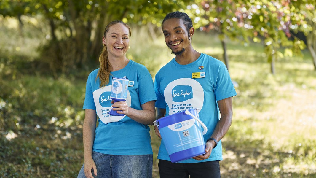 A male and female Sue Ryder fundraising volunteer, holding a collection tin and collection bucket