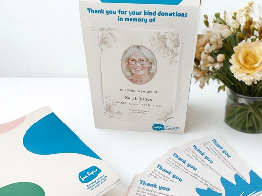 The Sue Ryder funeral pack, with collection box, donation envelopes and information pack, next to some flowers in a vase