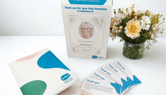 The Sue Ryder funeral pack, with collection box, donation envelopes and information pack, next to some flowers in a vase