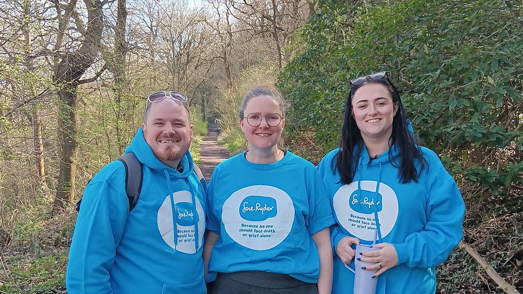 Three walkers in a forest, wearing blue Sue Ryder hoodies