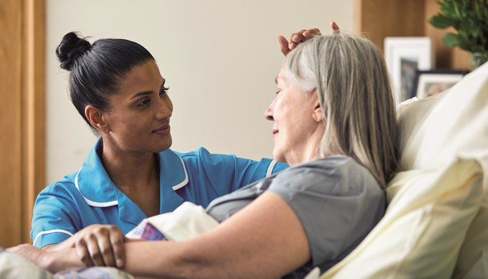 A Sue Ryder Nurse comforting a female patient at her bedside