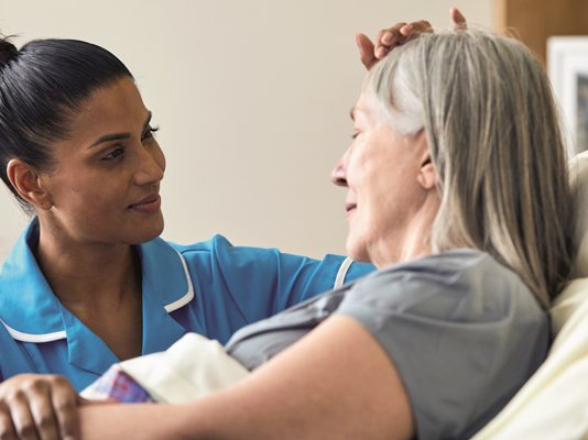 A Sue Ryder Nurse comforting a female patient at her bedside