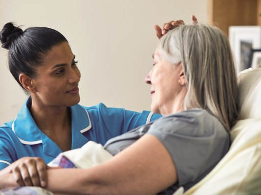 A Sue Ryder Nurse comforting a female patient at her bedside