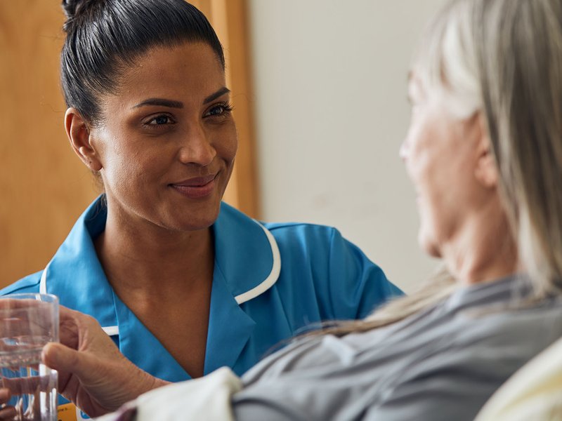 A Sue Ryder Nurse giving a patient a drink of water at their bedside
