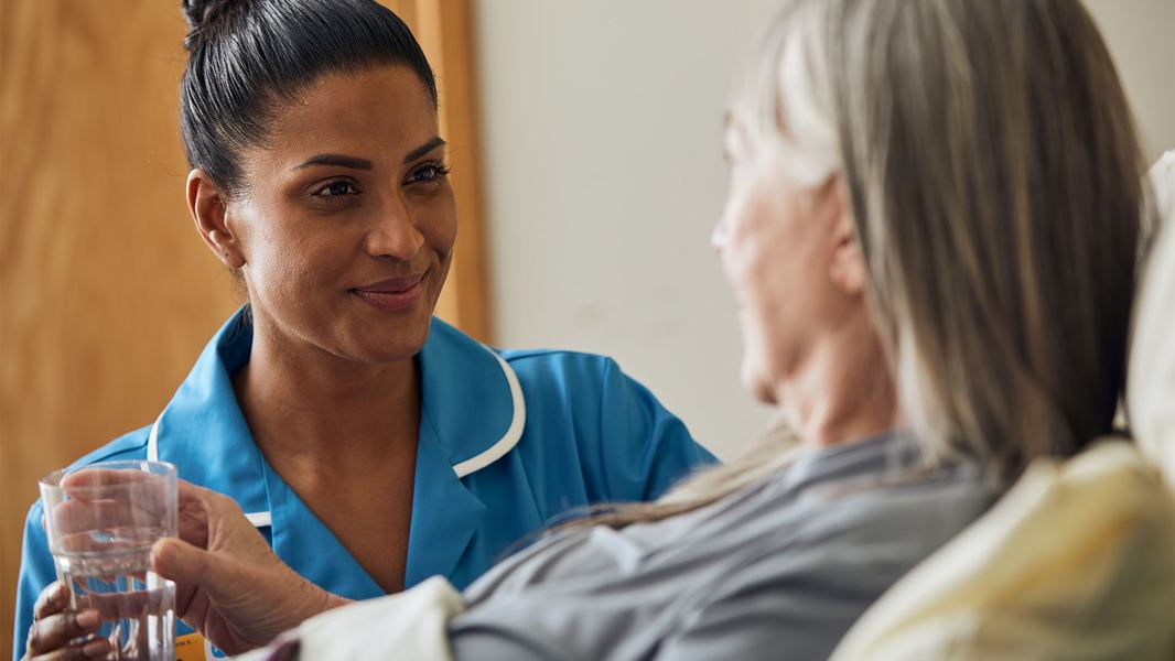 A Sue Ryder Nurse giving a patient a drink of water at their bedside