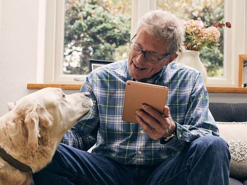An Online Community user at home on their tablet, smiling and stroking their dog