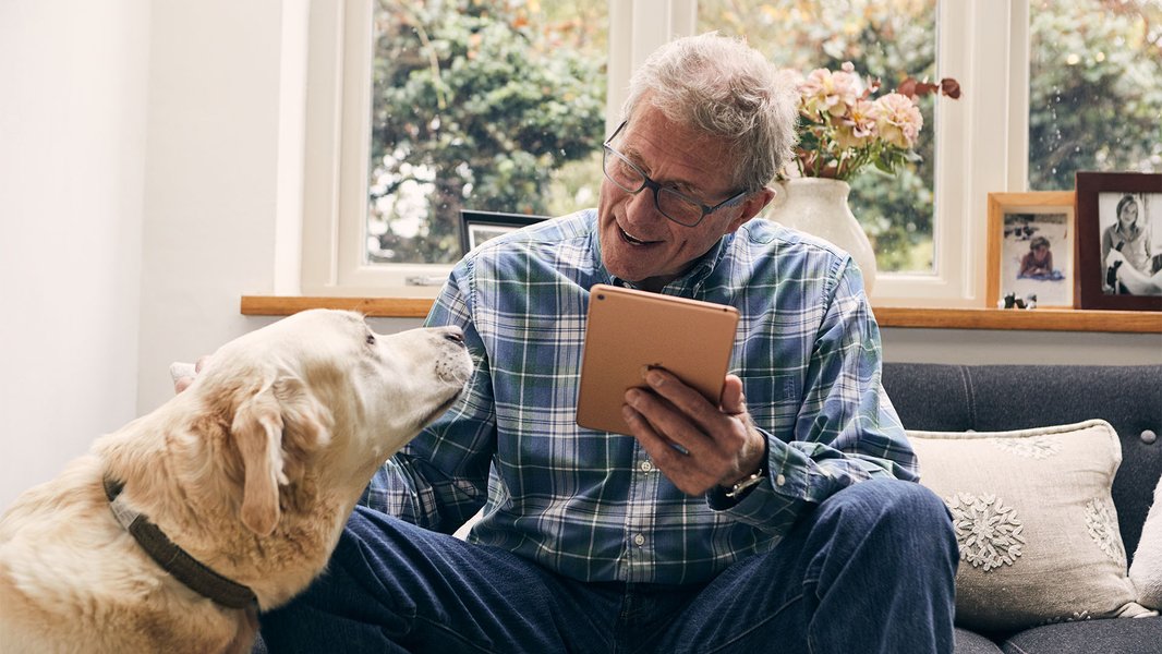 An Online Community user at home on their tablet, smiling and stroking their dog