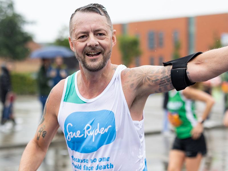A Sue Ryder runner racing in the rain, with his arm in the air celebrating