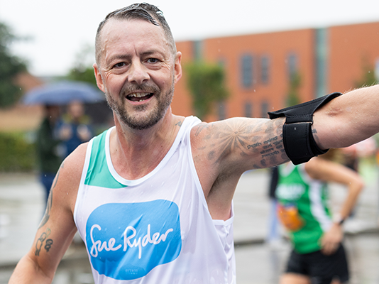 A Sue Ryder runner racing in the rain, with his arm in the air celebrating