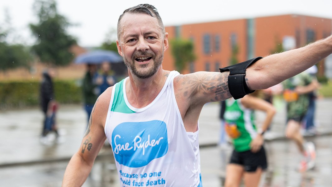 A Sue Ryder runner racing in the rain, with his arm in the air celebrating