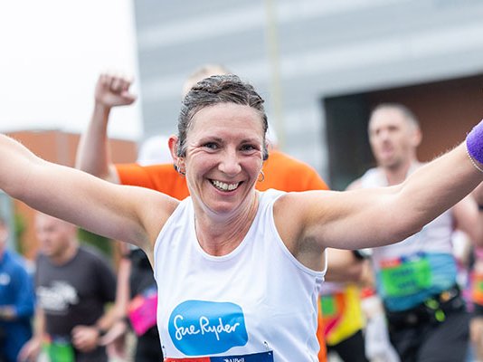 A smiling Sue Ryder runner with her hands in the air during the race