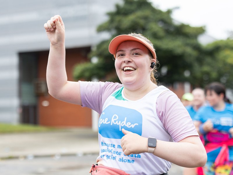 A smiling Sue Ryder runner holding her hand up in the air while racing
