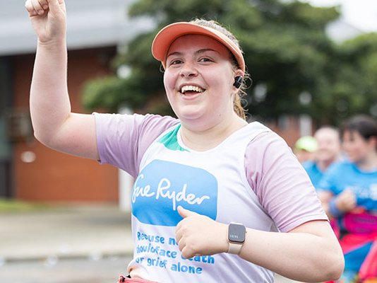 A smiling Sue Ryder runner holding her hand up in the air while racing