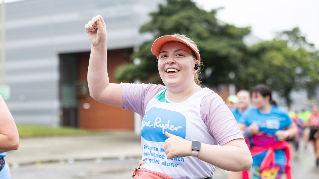 A smiling Sue Ryder runner holding her hand up in the air while racing