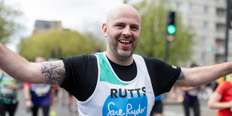A Sue Ryder runner on the race route, celebrating with their arms in the air